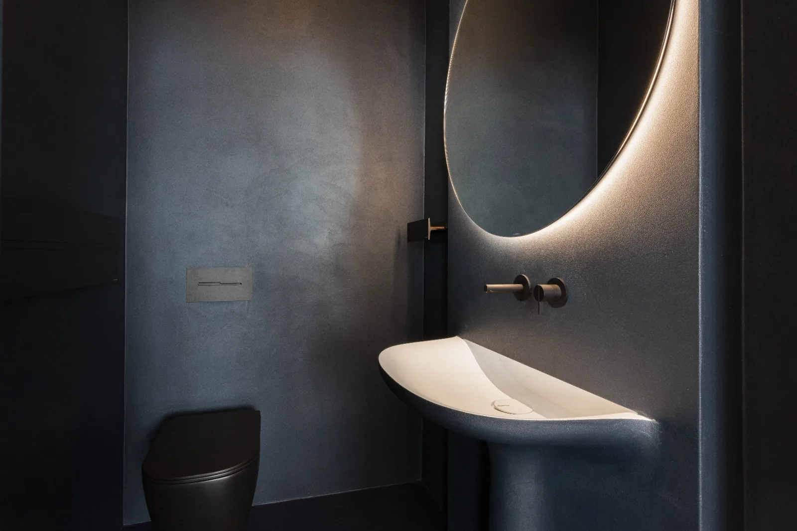 An ensuite in deep teal micro-cement with a sculpted basin
