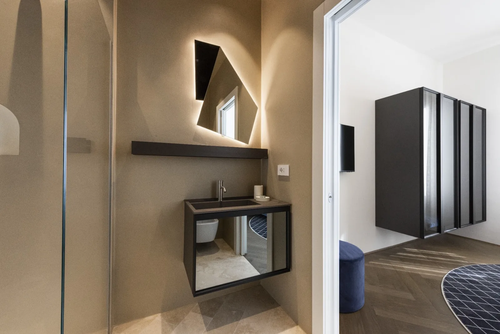 A second bath with a sculptural illuminated mirror and travertine floor