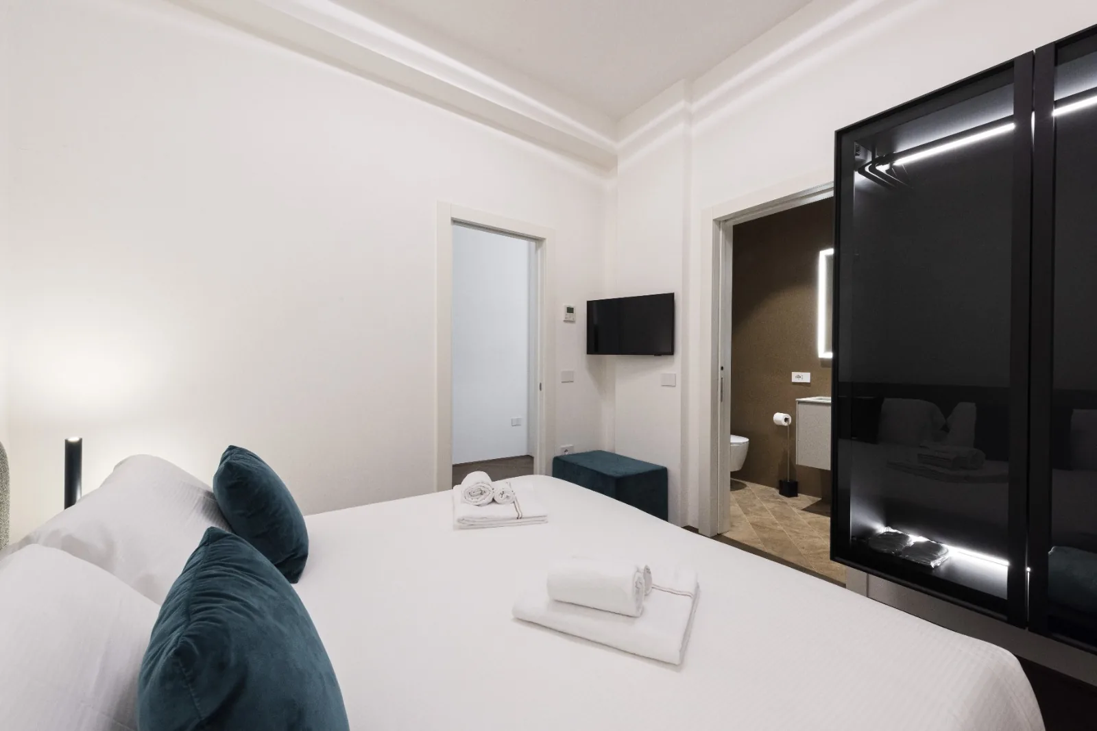 The second bedroom with teal velvet accents and a lit ensuite beyond
