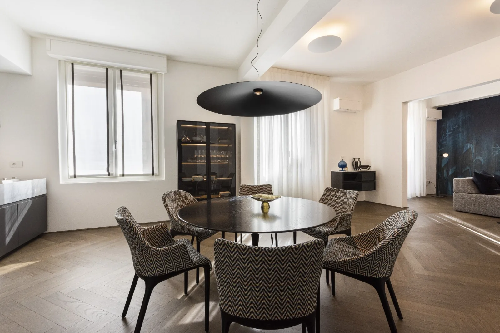 The dining area with a round black table and chevron upholstered chairs